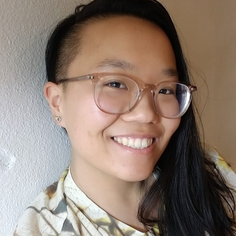 Selfie of a non-binary East Asian person with one side of their head shaved, wearing clear glasses