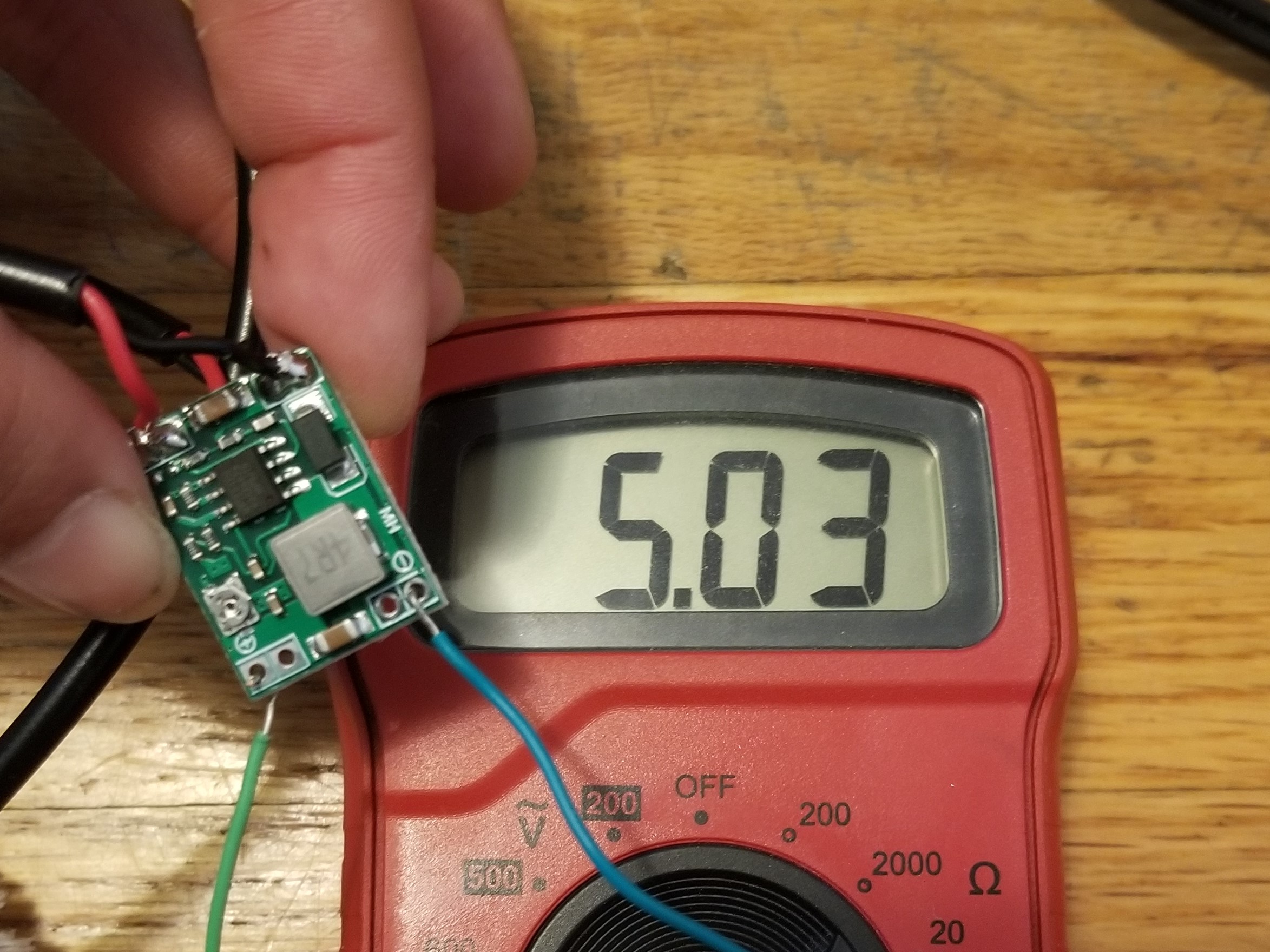 Cover image: a person holds a small voltage regulator PCB in front of a multimeter measuring its output voltage. The multimeter reads 5.03V.